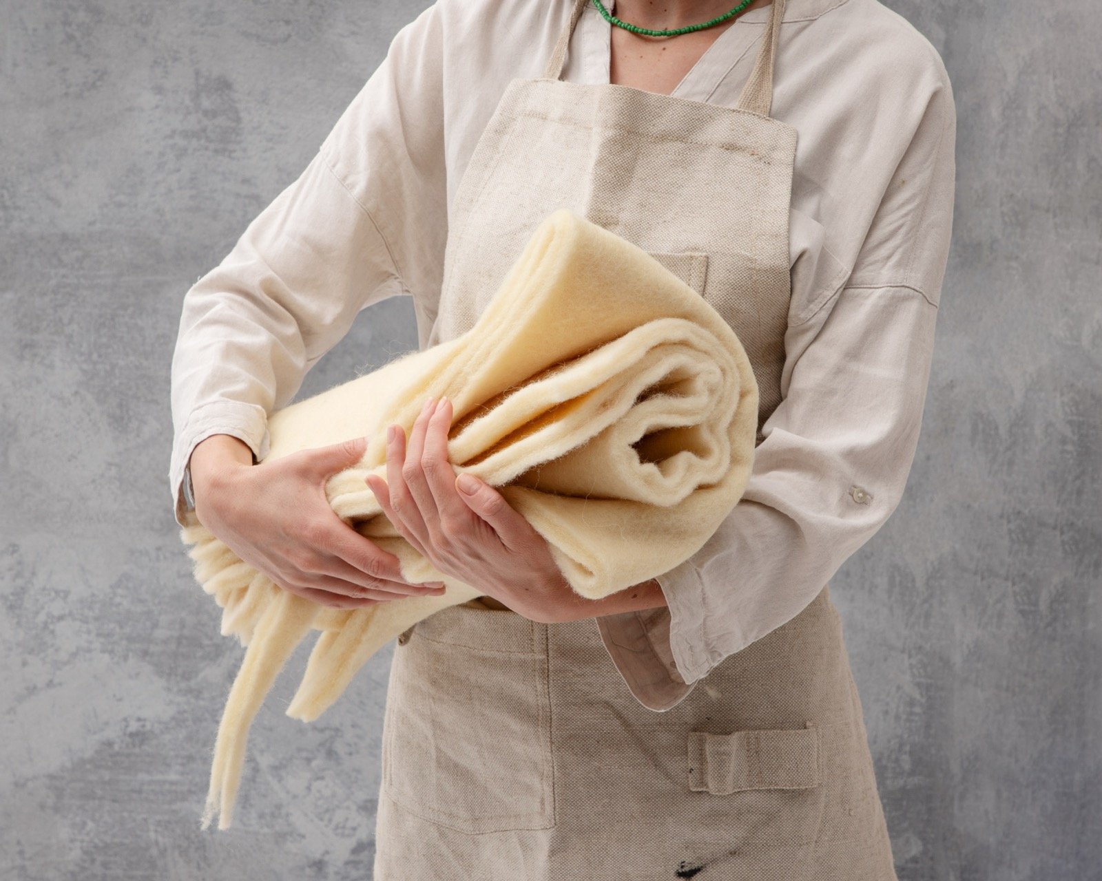 Artisan in a linen apron holding a rolled sheet of cream wool batting