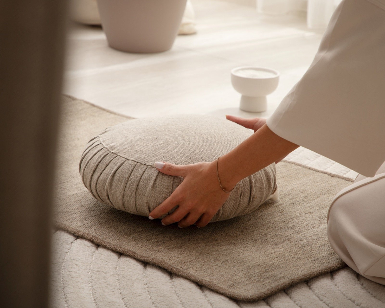 Hands placing a round linen meditation cushion on a wool rug