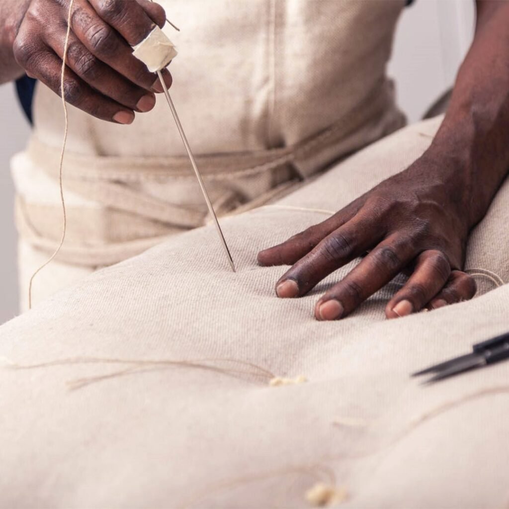 Hands tufting a wool mattress with a long needle and twine